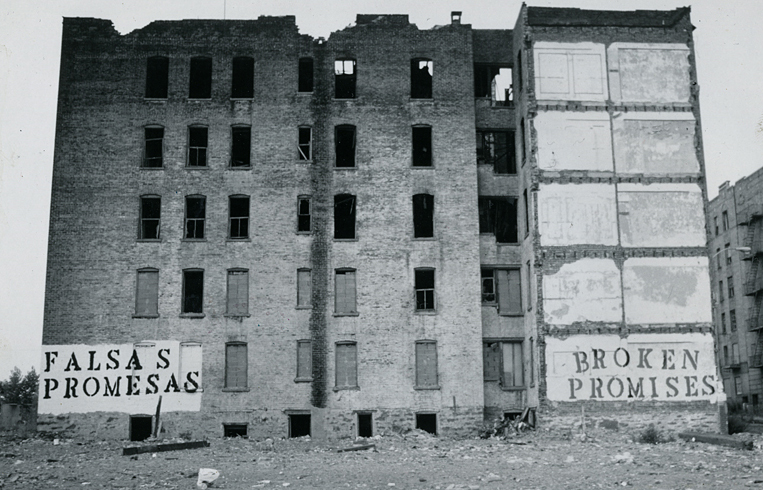 A gutted, abandoned five-story apartment building in the South Bronx with the words 'Falsas Promesas — Broken Promises' stenciled on its walls